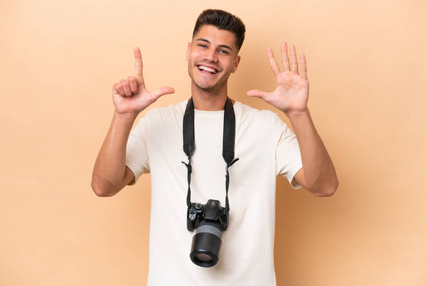 Jovem fotógrafo caucasiano isolado em fundo bege contando sete com os dedos - Foto, Imagem