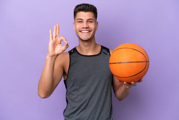 joven caucásico mujer baloncesto jugador hombre aislado en púrpura fondo mostrando ok signo con los dedos - Foto, Imagen