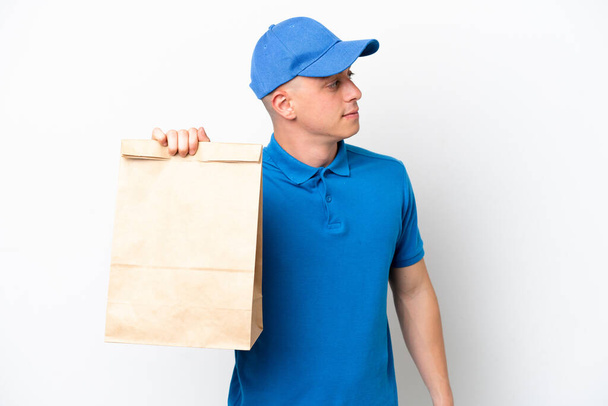 Young Brazilian man taking a bag of takeaway food isolated on white background looking to the side - Фото, зображення