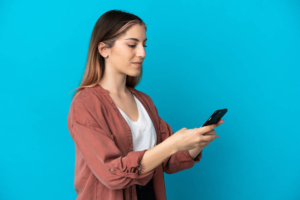 Młoda kaukaska kobieta odizolowana na niebieskim tle wysyłając wiadomość lub e-mail z telefonu komórkowego - Zdjęcie, obraz