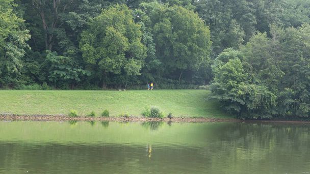 Una pareja jubilada irreconocible caminando junto a un lago con reflejos. - Foto, imagen
