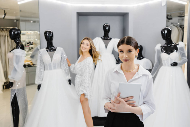 Atractivo dueño de la tienda nupcial mujeres utilizan tableta digital ayudar al cliente a elegir vestido de novia en la tienda. - Foto, imagen