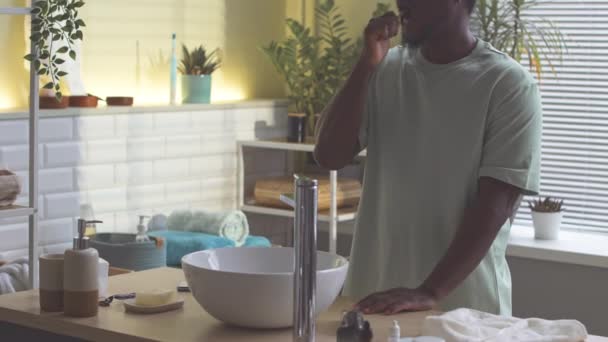 Przycięte zdjęcie Afroamerykanina stojącego przy zlewie w łazience myjącego zęby - Materiał filmowy, wideo