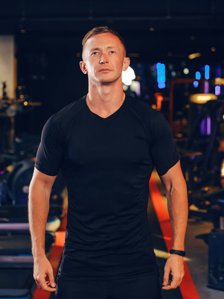 Muscular guy-athlete in a black T-shirt on the background of a fitness center or gym. Mockup, place for text. - Photo, Image