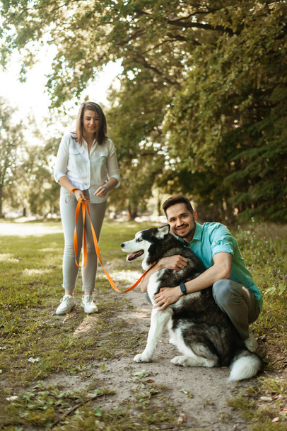 Joven pareja feliz con perro husky siberiano en el parque de verano. - Foto, imagen