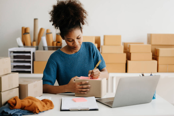 Startup small business SME, African woman entrepreneur checking online orders and preparing parcels for shipping - Foto, Bild
