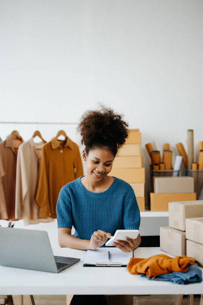 Startup small business SME. Entrepreneur African woman receiving and checking online orders. Young female small business owner packing parcels to ship them to customers - Φωτογραφία, εικόνα