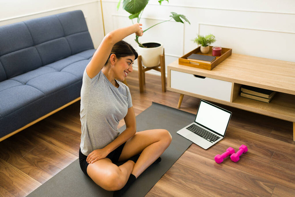 Активная молодая женщина занимается йогой дома и тренируется во время видео тренировки на пустом экране ноутбука с копировальным пространством - Фото, изображение