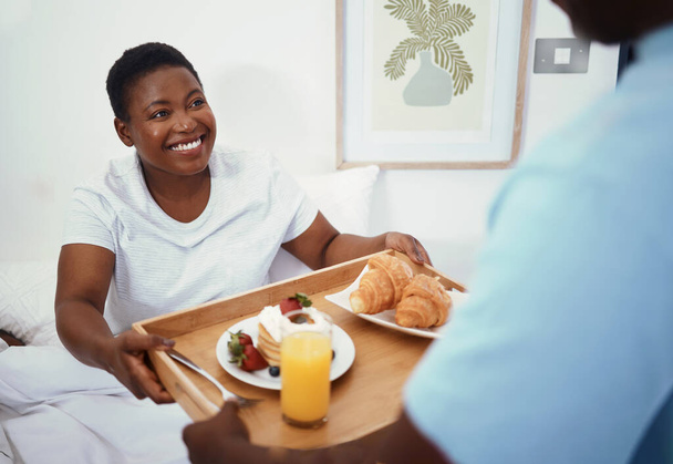 Happy, morning und ein schwarzes Paar mit Frühstück im Bett für Liebe, Pflege oder Geburtstag in einem Haus. Lächeln, Essen und ein afrikanischer Mann mit Essen für eine Frau im Schlafzimmer zusammen im Urlaub oder auf Hochzeitsreise. - Foto, Bild