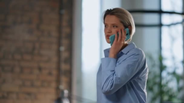 Nainen seisoo toimistossa sinisessä paidassa lähikuvassa. Itsevarma rikas liikenainen puhuu älypuhelin moderni yritys työpaikalla. Vakava naisjohtaja konsultoi asiakasta kännykällä. Liiketoiminta - Materiaali, video
