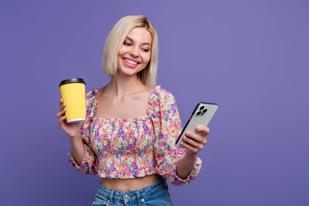 Portrait of charming lovely girl hold fresh coffee cup use smart phone empty space isolated on purple color background. - Foto, Imagem