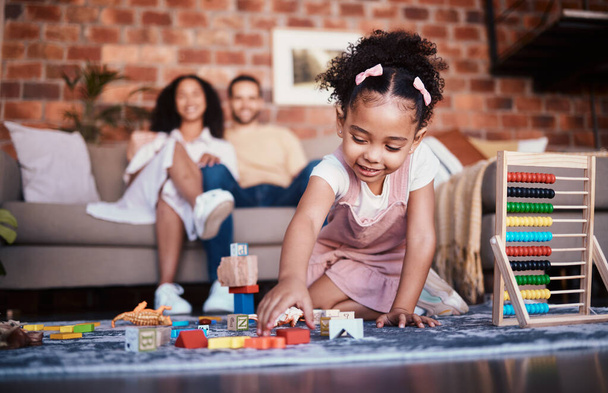 Child, toys and playing in home with development and building block in living room. Family, fun and youth learning with a young girl and parents in a house together with care and bonding education. - Photo, Image
