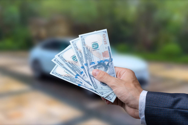 Un hombre con billetes de 100 dólares cerca del coche. Compra o alquila un auto nuevo. Concepto financiero - Foto, imagen
