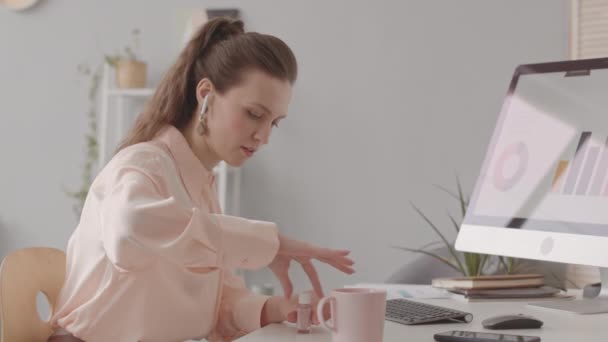 Joven mujer caucásica pintándose las uñas por computadora de escritorio en el escritorio de la oficina - Metraje, vídeo