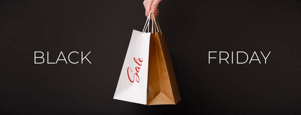 ブラックフライデーセールバナー。 黒い背景に2つのショッピングバッグを保持する女性の手 - 写真・画像