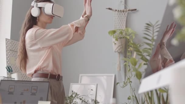 Giovane donna che indossa auricolare vr gesticolare con le mani mentre sperimenta la realtà virtuale sul posto di lavoro in ufficio - Filmati, video