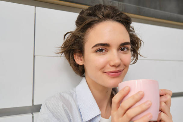 Gros plan portrait de belle fille, boit du café, tient une tasse de thé et sourit à la caméra, s'assoit et se réaligne avec du cacao. - Photo, image
