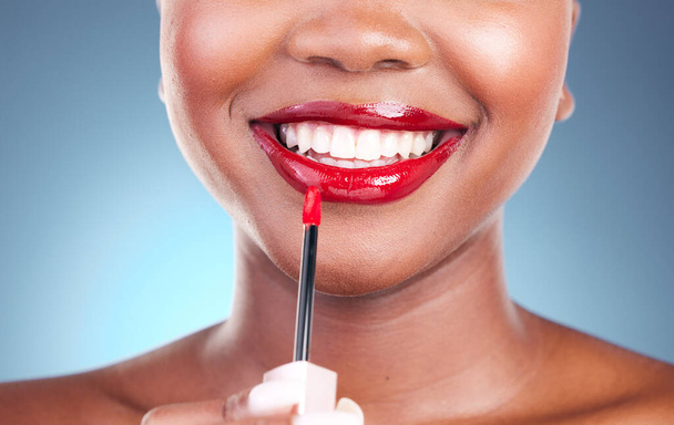 Γυναίκα, χαμόγελο και κόκκινο κραγιόν με πινέλο και ομορφιά, χαρούμενος με το μακιγιάζ closeup απομονώνονται σε μπλε φόντο. Μοντέλο, τολμηρό και καλλυντικό προϊόν σε χείλη, στόμα με δέρμα και δόντια με λάμψη στο studio. - Φωτογραφία, εικόνα