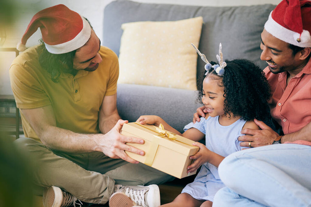 Γκέι, Χριστούγεννα και ένας πατέρας με ένα δώρο για ένα παιδί, γιορτή και διακοπές ως οικογένεια. Χαμογελάστε, σπίτι και ένας άνδρας της Igbt με ένα γιορτινό δώρο για ένα κορίτσι στο σαλόνι ενός σπιτιού μαζί. - Φωτογραφία, εικόνα