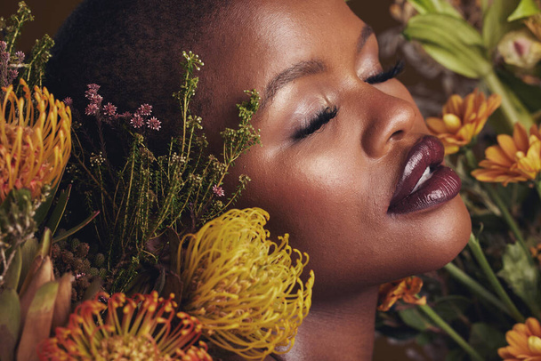 Μαύρη γυναίκα, λουλούδια και ομορφιά με πρόσωπο, μακιγιάζ και φυσική καλλυντική φροντίδα που απομονώνεται στο φόντο του στούντιο. Αφρικανικό μοντέλο, φυτά και φύση με βιώσιμη περιποίηση της επιδερμίδας, μάτια κλειστά με πρόσωπο και λάμψη. - Φωτογραφία, εικόνα