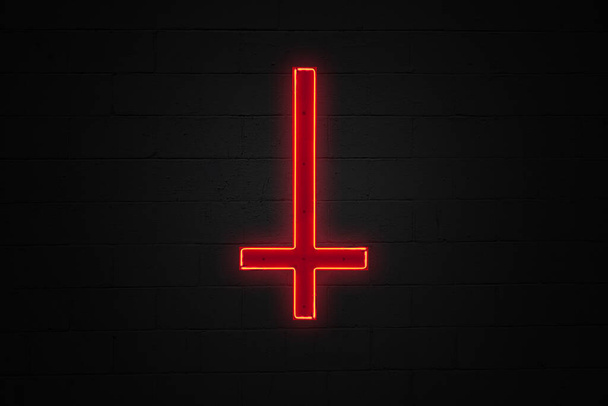 Luz de neón en forma de cruz roja al revés de San Pedro unida en medio de una pared de ladrillo. - Foto, imagen