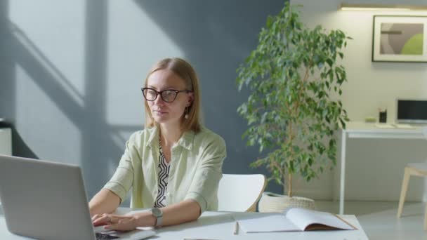 Portrait of businesswoman working on laptop and then posing for camera with smile at desk in comfortable office - Footage, Video