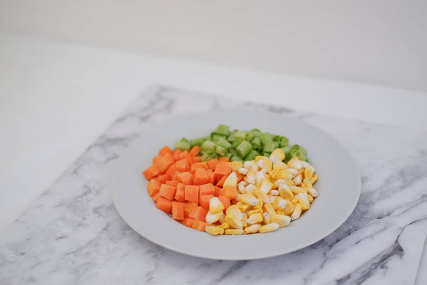 Frozen vegetables on a white plate on a white marble table. - Photo, Image