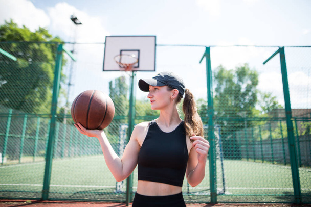 Young sports girl with a basketball on the basketball court outdoors, active weekend. - Photo, Image