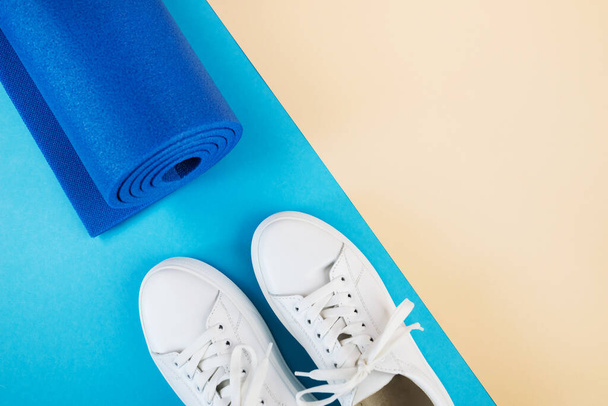 Foto de vista superior de zapatillas blancas y alfombra de fitness. El concepto de deporte, yoga, fitness. - Foto, Imagen