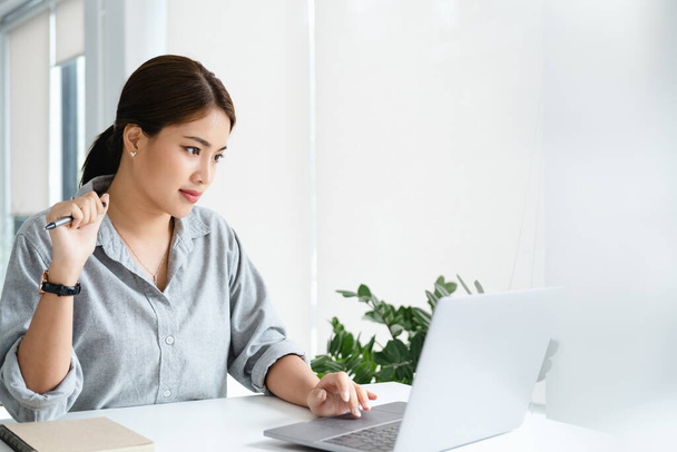 Concentrated young beautiful businesswoman working on laptop in bright modern office - Photo, image