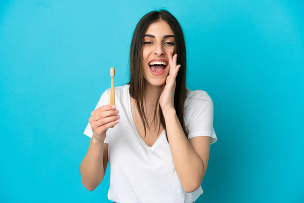 Молодая белая женщина чистила зубы на синем фоне, крича с широко раскрытым ртом - Фото, изображение