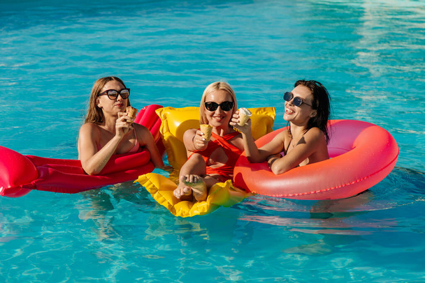 Μια ομάδα όμορφων, νεαρών γυναικών τρώνε γρανίτες φράουλας και διασκεδάζουν στην πισίνα. - Φωτογραφία, εικόνα
