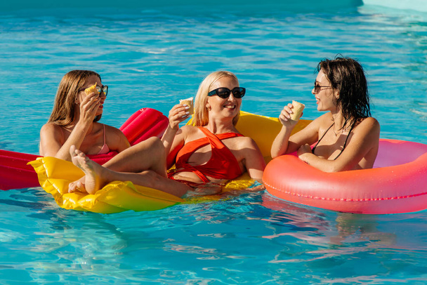 Ryhmä kauniita, nuoria naisia syö mansikkamehujäitä ja pitää hauskaa altaassa.. - Valokuva, kuva