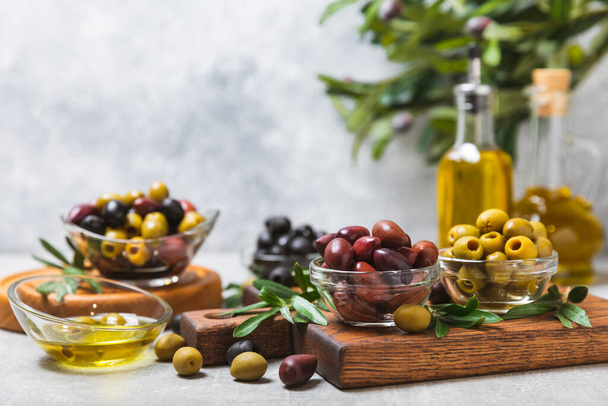 A set of green, red and black olives on a light marble background. Various types of olives in bowls and fresh olive leaves. Vegan. Olive fruits. Place for text. Copy space. - Photo, Image
