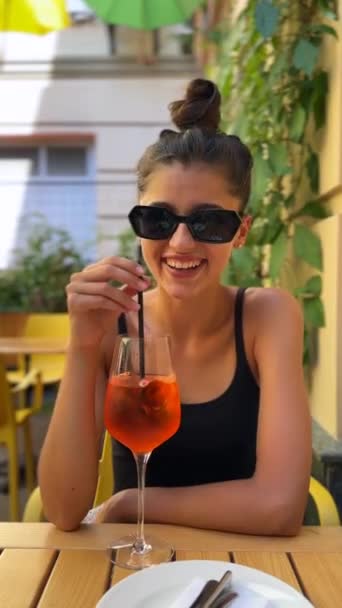 Een charmant, jong meisje nipt Aperol op het terras van het restaurant. Hoge kwaliteit 4k beeldmateriaal - Video