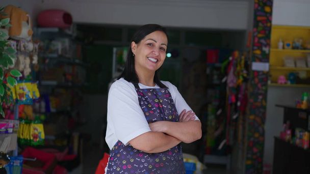 Χαρούμενη γυναίκα Pet Shop Ιδιοκτήτης στην Apron Αφίσες για Κάμερα με σταυρωμένα τα χέρια. Σίγουρος ιδιοκτήτης μικρών επιχειρήσεων από τη Νότια Αμερική - Φωτογραφία, εικόνα