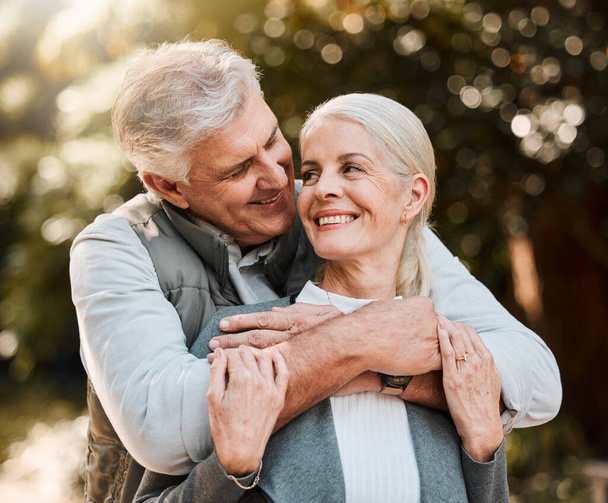 Love, hug and senior couple at a park happy, free and enjoy travel, holiday or weekend outdoor. Face, smile and elderly man embrace woman in forest, bond and having fun on retirement trip together. - Foto, afbeelding