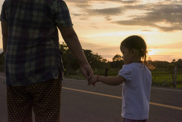 Een kind dat de hand van zijn moeder vasthoudt als de zon ondergaat Ouders en kinderen tonen hun pure liefde voor elkaar door op een zonnige straat te staan. - Foto, afbeelding