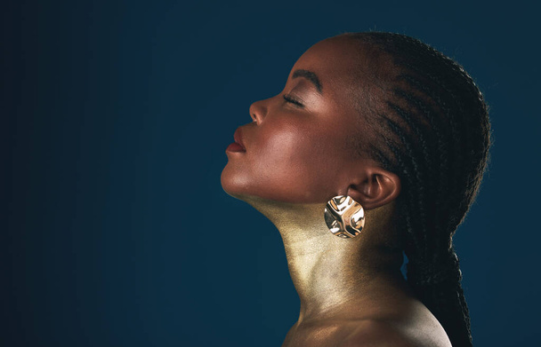Profile, beauty and black woman in gold for culture, heritage or tradition on a blue background in studio. Face, mockup and african style with a young model closeup for elegance or cosmetics. - Photo, Image