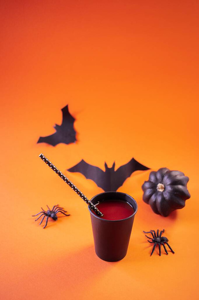 Cadılar Bayramı, kırmızı içki, kokteyl, siyah bardaklarda, yarasalar ve örümcekler turuncu arka planda - Fotoğraf, Görsel