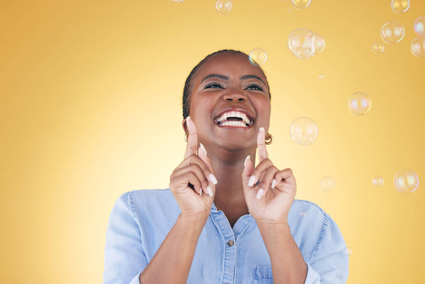 Aufgeregte, glückliche und schwarze Frau auf gelbem Hintergrund mit Blasen für Glück, Freude und Spaß. Verspieltes Lachen, Lächeln und isolierte afrikanische Person im Studio mit Seifenblase für Freiheit, Magie und Farbe. - Foto, Bild