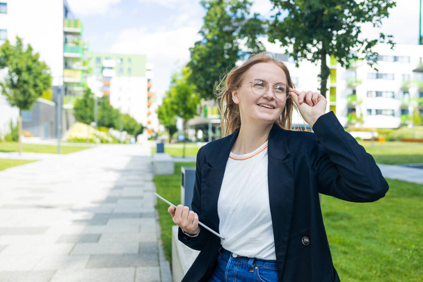 Retrato de una joven joven y sonriente mujer de negocios al aire libre sosteniendo una tableta con expresión feliz. Foto de alta calidad - Foto, Imagen