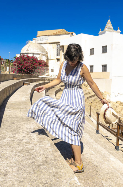 Blanke toeristenvrouw met een zomerjurk en een vintage strohoed terwijl ze geniet van een bezoek aan de resten van het Romeinse theater van Cadiz, Andalusië, Spanje. - Foto, afbeelding