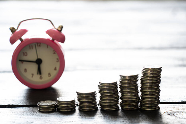 Stapel von Münzen stehen auf einem Holztisch und ein Wecker steht in der Nähe, Wirtschaft und Finanzen, Erfolgszeit - Foto, Bild