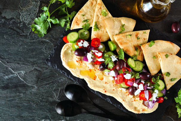 Hummus dip schotel met pita en verse groenten. Bovenaanzicht tafelscène met een donkere leisteen achtergrond. - Foto, afbeelding