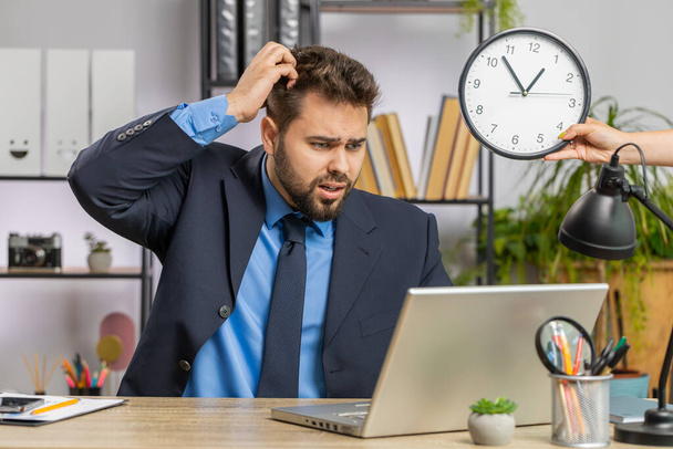 Homme d'affaires caucasien travaillant sur ordinateur portable de bureau avec l'anxiété vérifier le temps sur l'horloge en retard au travail étant dans le délai de retard. Manager freelance homme regardant heure, minutes inquiétant d'être ponctuel - Photo, image