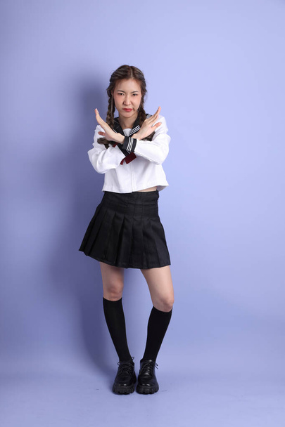 Das asiatische Mädchen in japanischer Studentenuniform steht auf dem lila Hintergrund. - Foto, Bild
