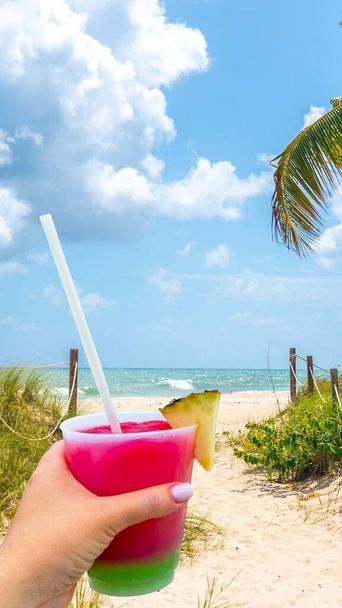 Tenendo in mano un bicchiere con cocktail e paglia e Sand Path andando verso l'oceano a Miami Beach, Florida negli Stati Uniti - Foto, immagini