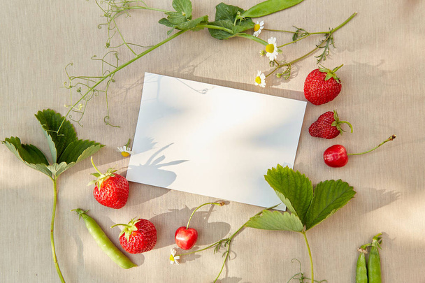 Stationery card mockup under hard shadows outside among strawberry, cherry and camomiles outside. Cottagecore, naturecore lifestyle top view. - Photo, Image