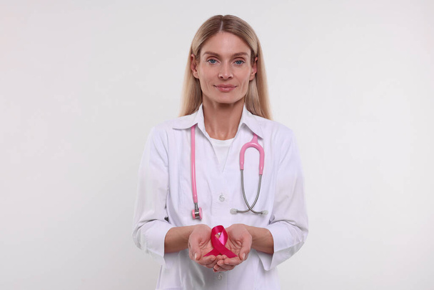 Doctor with stethoscope holding pink ribbon on white background. Breast cancer awareness - Fotografie, Obrázek